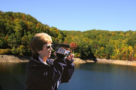 Tourist taking in the Fall colors surrounding the lake with her camcorder in hand.の写真素材