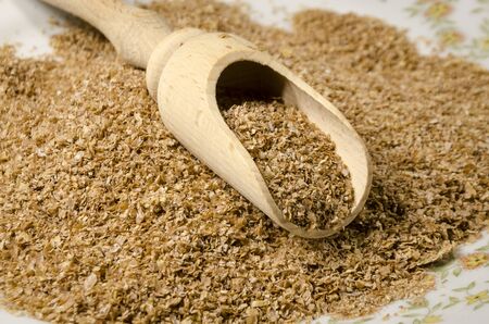 raw bran on a white plate with woodden scoopの写真素材