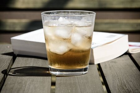 Cold drink with ice cubes on a wooden terrace table