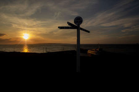 The sun setting behind the iconic signpost at John O'Groats in the Scottish Highlands, UK