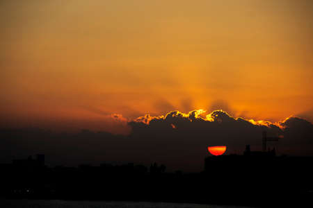 The sun slips behind the clouds with an orange sky in the Mediterranean Seaの写真素材
