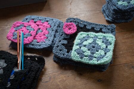 hand made crochet granny squares with crochet hooks on wooden table.