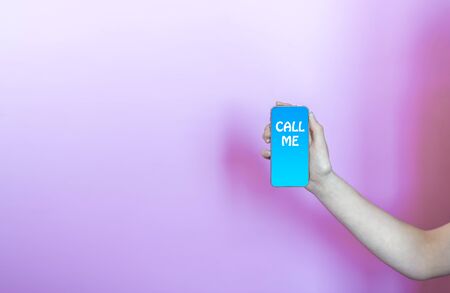young womans arm & hand holding smartphone with call me written on the screen with pink background; with room for text.の写真素材