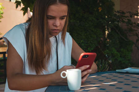 young woman in the garden with mobile phone, studying or relaxing. wearing shorts and tshirt. , sitting at table.の写真素材