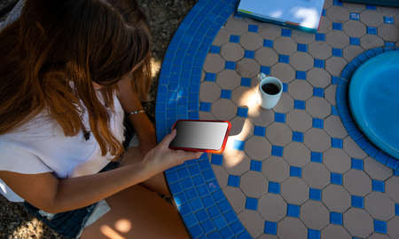 young woman in the garden with mobile phone, studying or relaxing. wearing shorts and tshirt. ,...
