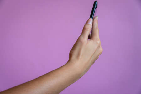 female hand holding mobile phone against a pink, mauve background. Room for textの写真素材