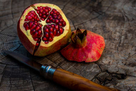 Cut open Pomegranate showing colouful seeds on rustic wooden table with french folding Knife.の写真素材