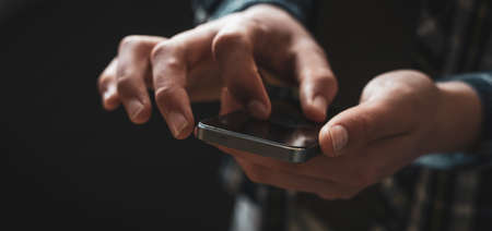 man using mobile phone, dark background wide image. focus on phone.