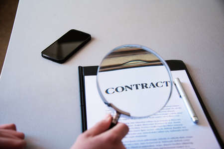 young man looking at contact with a magnifying glass, checking the small print, house buying or working from home; selective focusの写真素材