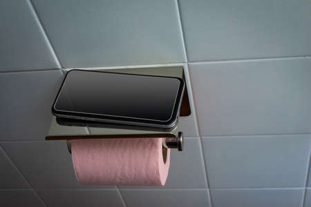 Mobile phone in toilet with pink toilet paper against white tile background .concept addiction to...