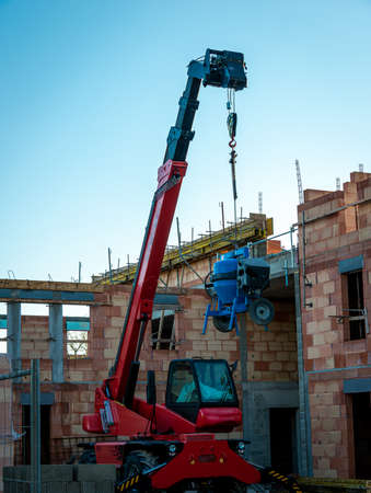 Blue cement or concrete mixer hanging from red telescopic fork lift truck on a french building site, anti theftの写真素材