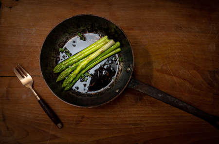 asparagus spears in frying pan on wooden chopping board, good food, healthy eating.