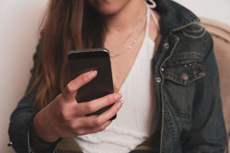 Young woman looking at mobile telephone sending text messages and surfing the internet.