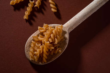 whole meal Fusilli pasta in wooden spoon on dark background.の写真素材