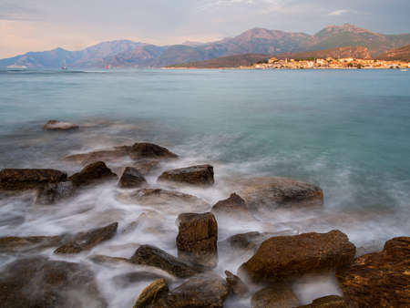 seascape of rocks going into the Mediterranean sea with the town of Saint Florent, Corsica, France in the distance. holiday destinations.の写真素材