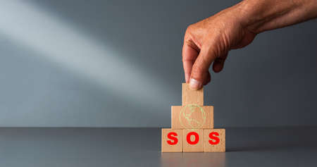 save the planet concept ,wooden blocks with green planet and SOS in red , with gray background , room for your text .の写真素材