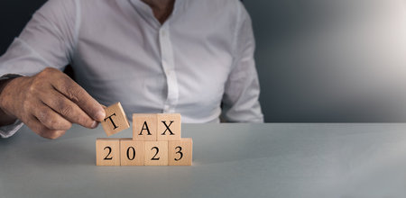 Man posing wooden blocks with tax 2023 concept of tax year and budget on gray blue background with copy space.の写真素材