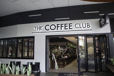 Tweed Heads NSW Australia, may 24 2019: Coffee club front with a black writing sign on a white tiles background. Plants out the front with seats pople and chairs on the insideのeditorial素材