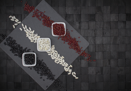 Background design composition from above with square slate plate and three bowls with beans of...