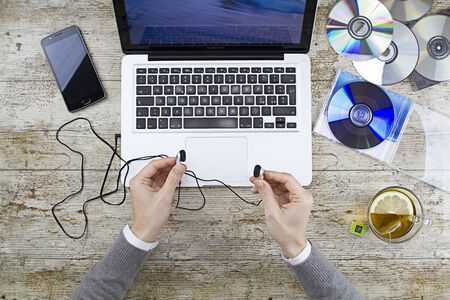 Young woman shooting from above working on laptop on wooden table listening to music cd with a cup...