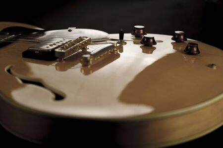 Vintage archtop guitar in natural maple close-up high angle view on black background, controls...