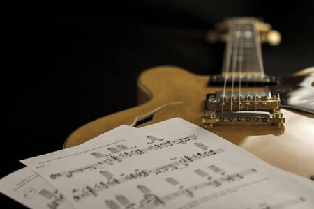 Vintage archtop guitar in natural maple close-up high angle view with music sheets on black backgroundの写真素材