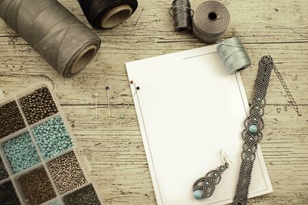 Top view of a wooden table with tools, spools of thread, natural stones and colored beads to make...