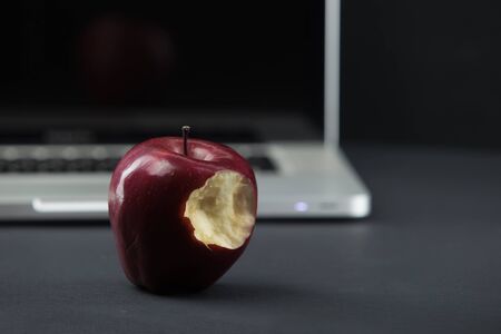 Shiny red apple resting on an open aluminum laptop in selective focus on a black backgroundの写真素材