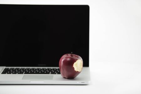 Shiny red apple resting on an open aluminum laptop in selective focus on a black backgroundの写真素材