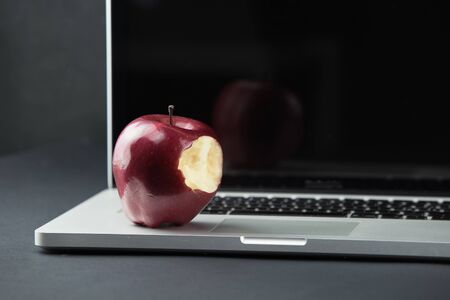 Shiny red apple resting on an open aluminum laptop in selective focus on a black backgroundの写真素材