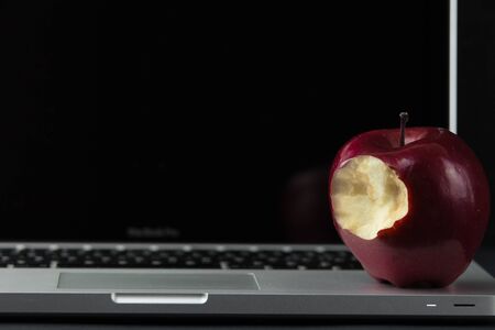Shiny red apple resting on an open aluminum laptop in selective focus on a black backgroundの写真素材