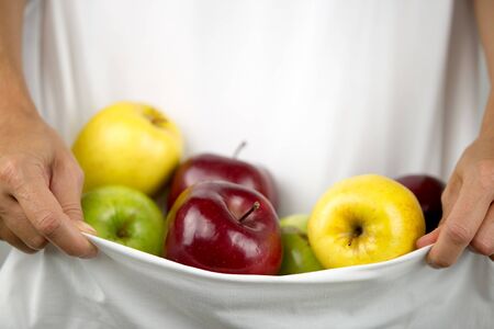 A Caucasian woman holds some apples of various types and colors in her white dress clasped in her handsの写真素材