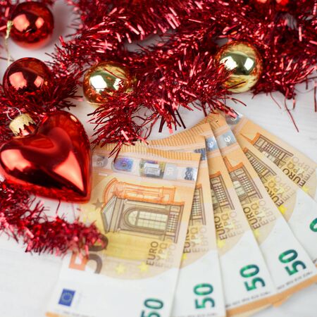 Christmas money business concept: some fifty euro banknotes with red and gold baubles and wreath decoration on light wooden tableの写真素材