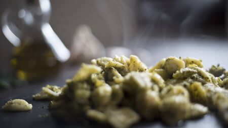 Closeup of a slate plate with steaming orecchiette with broccoli, typical Apulian recipe, in backlight on dark wooden table with olive oil and garlic on background in bokeh effectの写真素材