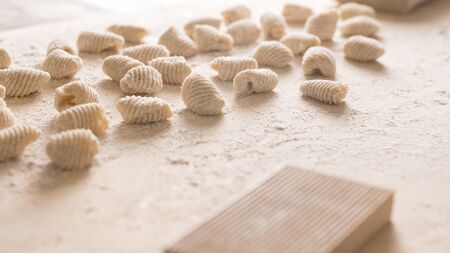 Close up of homemade vegan gnocchi pasta with wholemeal flour on the wooden chopping board with back light morning sunlight bokeh effect, traditional Italian pastaの写真素材
