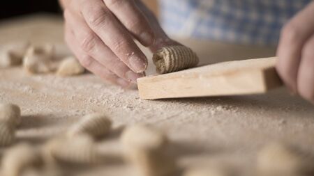 Close up process of homemade vegan gnocchi pasta with wholemeal flour making. The home cook crawls on the special wooden tool the gnocco , traditional Italian pasta, woman cooks food in the kitchenの写真素材