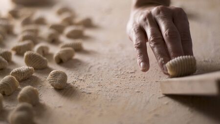 Close up process of homemade vegan gnocchi pasta with wholemeal flour making. The home cook crawls on the special wooden tool the gnocco , traditional Italian pasta, woman cooks food in the kitchenの写真素材