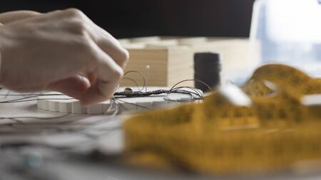 Lifestyle concept, work from home to reinvent your life: close-up of woman hands making macrame knotted jewelry with stone beads and tools on light wooden tableの写真素材