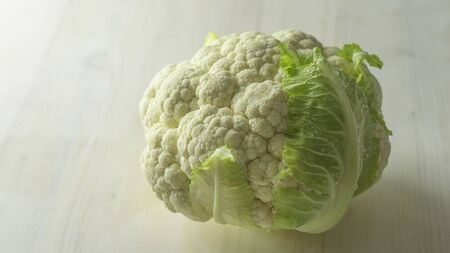Close-up studio shot of a freshly harvested cauliflower cabbage with green leaves that surround it...