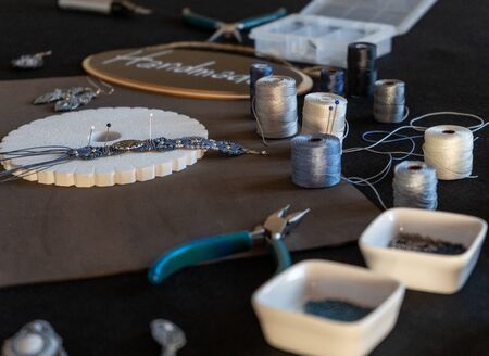 Lifestyle concept, work from home to reinvent your life: close-up of handmade macrame bracelet with specific tools, kumihimo, spools of thread in foreground and bokeh effectの写真素材