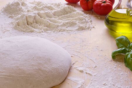 Macro close up of bread or pizza dough on wooden worktop and flour, extra virgin oil, tomatoes and basil in the backgroundの写真素材