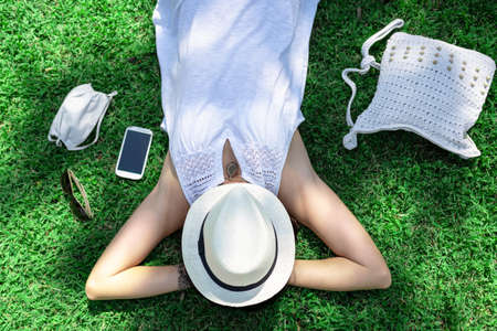 Top view of a Caucasian woman resting lying on a green field of the park with the face covered by...
