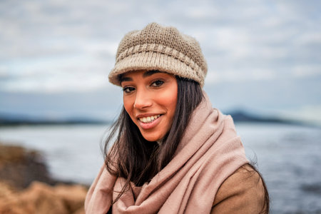 Cute Hispanic young woman with long black hair looking at camera posing outdoor in sea resort with...