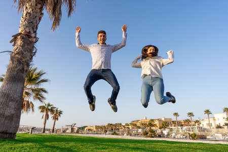 Happy people rejoice in the success of life jumping in air with open arms looking at the camera. Two...