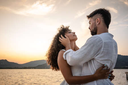 Romantic scene of bearded macho man holding head of his beautiful curly African-American woman in his hands looking into her eyes. Sentimental scene of young couple in love at sunset in natureの写真素材