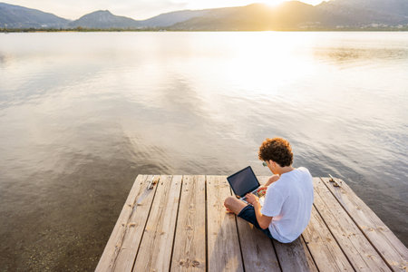 Nerd guy spending time outdoor programming at sunset writing code using laptop. New job opportunity at modern times to work everywhere using notebook and wifi 5g or 4g internet connection technologyの写真素材