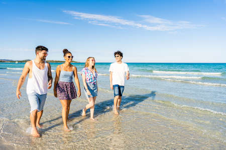 Multicultural friends walking in summer beach vacation in crystal clear water of tropical ocean sea resort smiling wearing casual clothes. Multiracial millennial happy people enjoying life in natureの写真素材