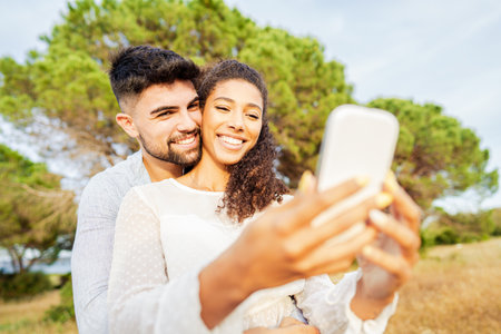 Young beautiful multiracial couple in love taking selfie in nature enjoying vacation moments sharing photos on social networks.の写真素材