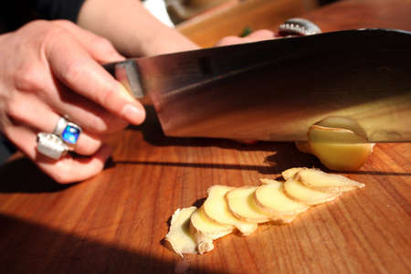 Slicing ginger on a wooden chop block.の写真素材