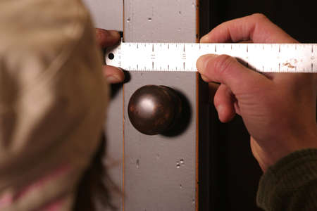 A cabinet maker measures a door stile with a ruler.